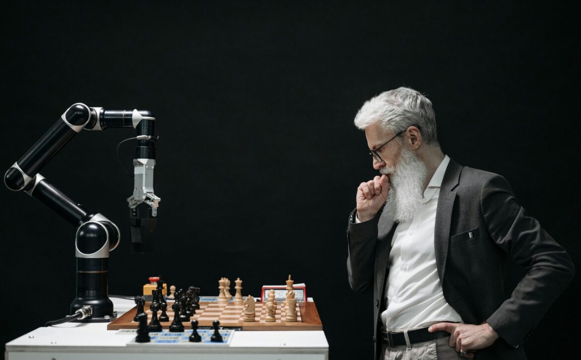 An elderly scientist contemplates a chess move against a robotic arm on a chessboard.