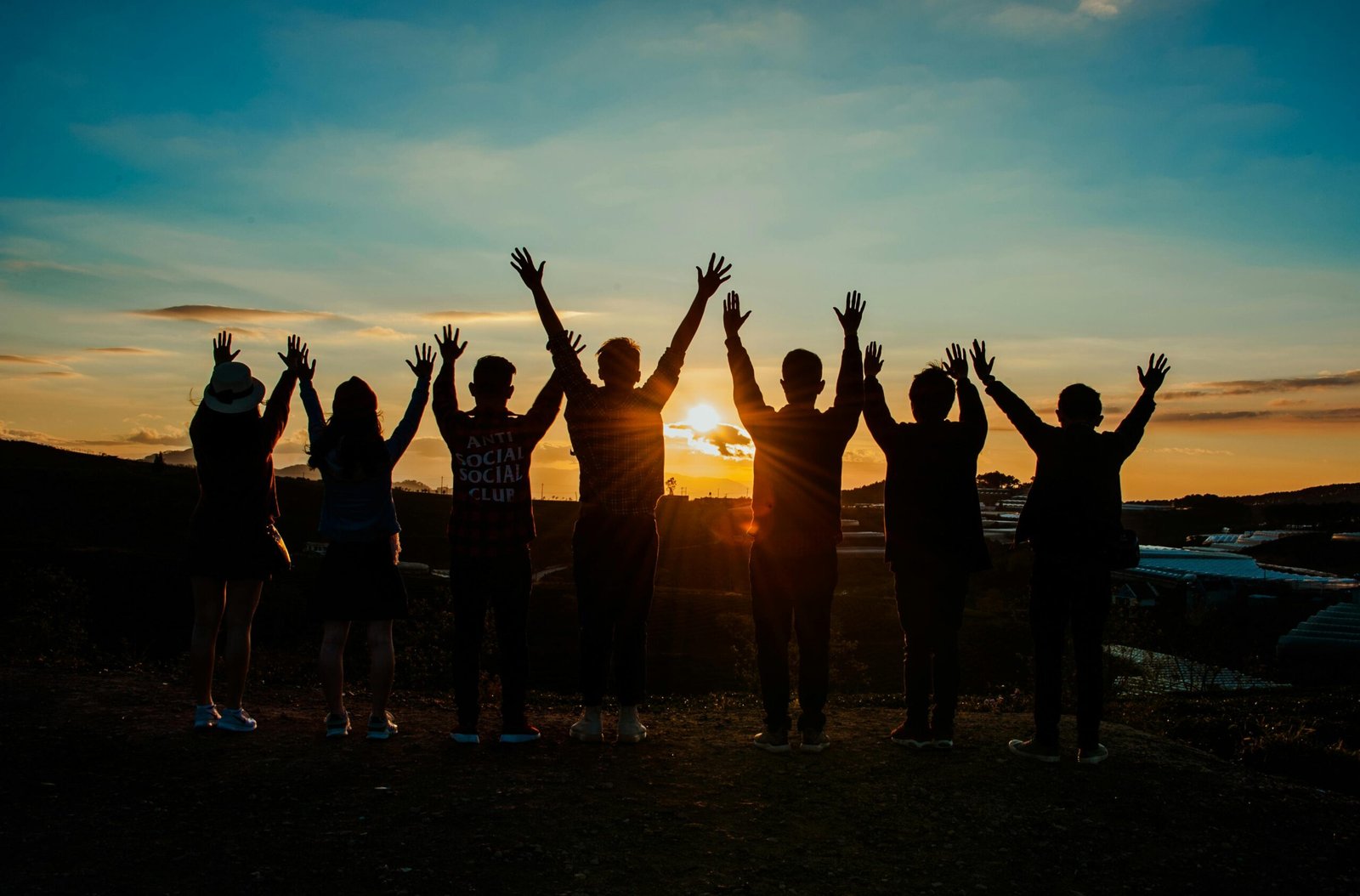 Menschen stehen bei Sonnenuntergang zusammen und heben die Arme